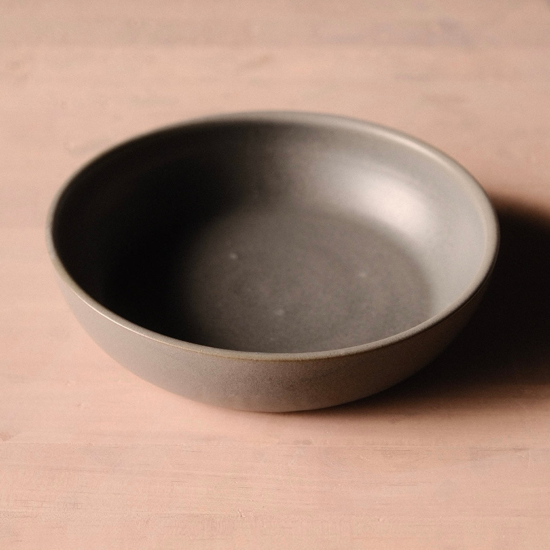Low, wide grey Wander Dinner Bowl photographed alone on a pale tabletop.